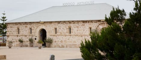 A stone building with the name 'KIDOGO ARTHOUSE' on the roof, surrounded by a fenced area with potted plants.