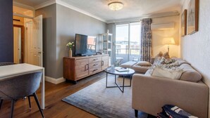 A modern living room with a sofa, coffee table, TV, and a view of the city through large windows. - Central Hidden Gem - Fremantle Apartment (Fremantle)