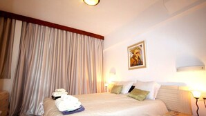 Une chambre d’hôtel avec un lit, des rideaux, un tableau et une table de chevet avec une lampe.