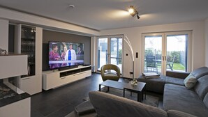 A modern living room with a flat-screen TV, a sofa, a coffee table, and a dining area. - House Comfort, with outdoor whirlpool and sauna for exclusive use, 300m to the lake (Göhren-Lebbin)