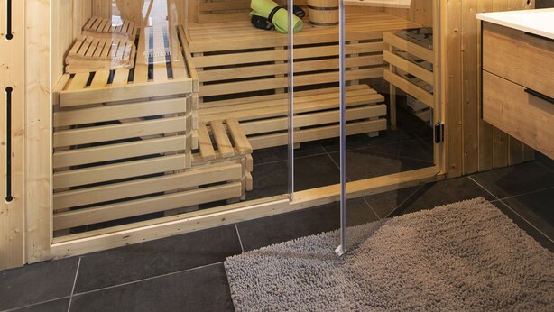 A sauna room with wooden benches, a glass door, and a small table with a towel. - House Comfort, with outdoor whirlpool and sauna for exclusive use, 300m to the lake (Göhren-Lebbin)