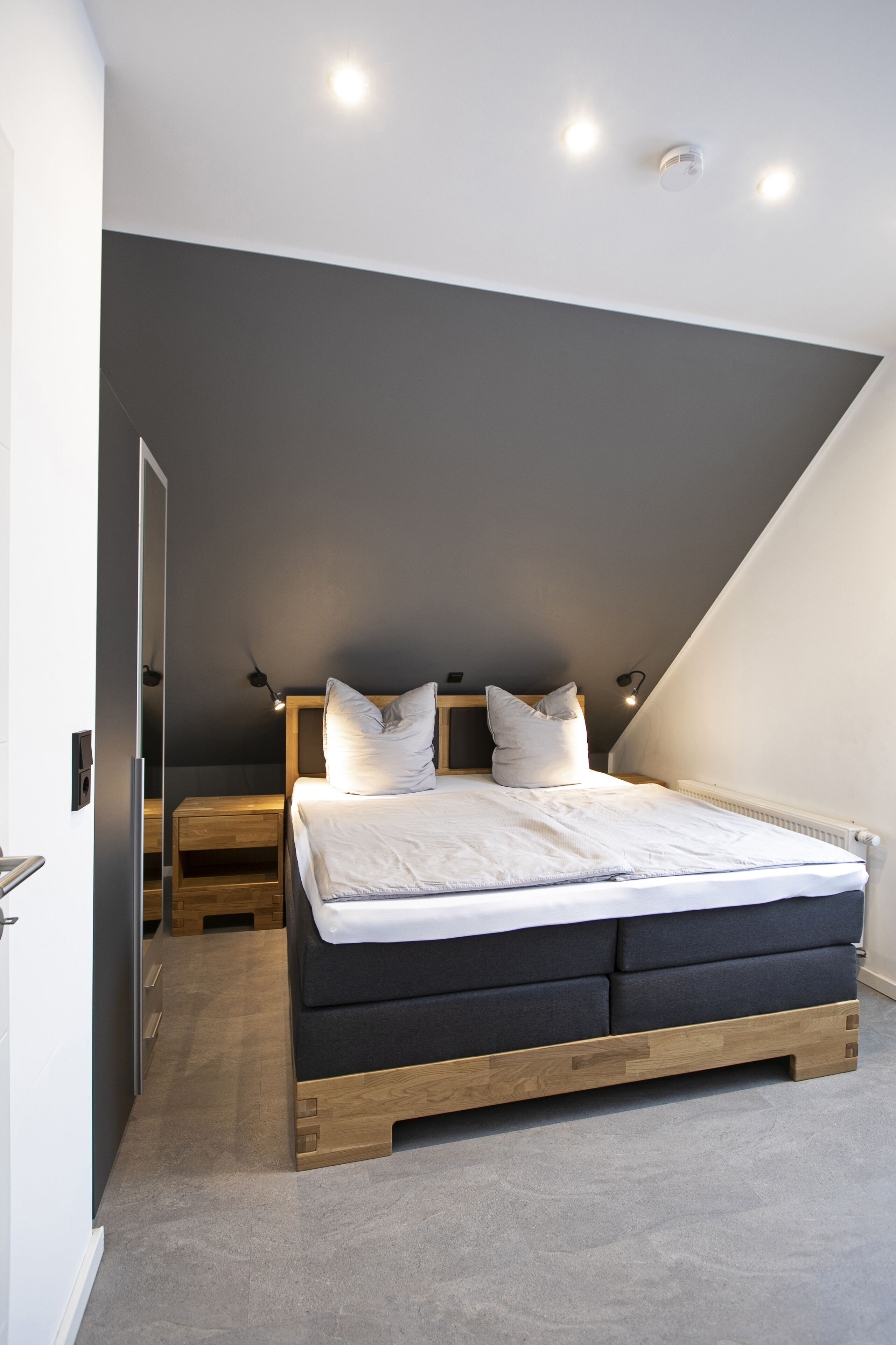 Un dormitorio con una cama, mesitas de noche y techo inclinado.