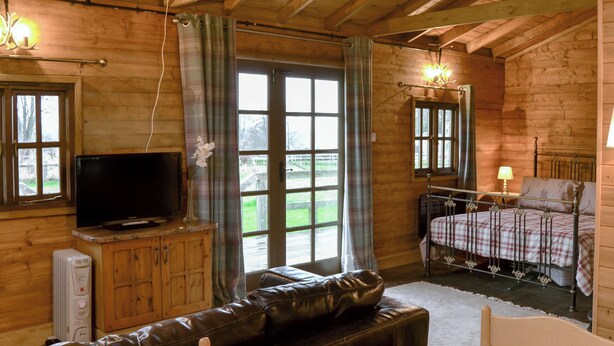 Une pièce chaleureuse aménagée dans un chalet en bois, avec une télévision, un canapé, un lit avec un cadre en métal et une table à manger pour deux personnes.