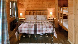 Une chambre dans une cabane en bois, avec un lit, deux lampes de chevet, une fenêtre et un lit superposé.