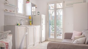 Una cucina compatta con mobili bianchi, un lavello e un frigorifero. È presente una zona pranzo con tavolo e sedie, e una porta scorrevole in vetro che dà su un patio esterno.