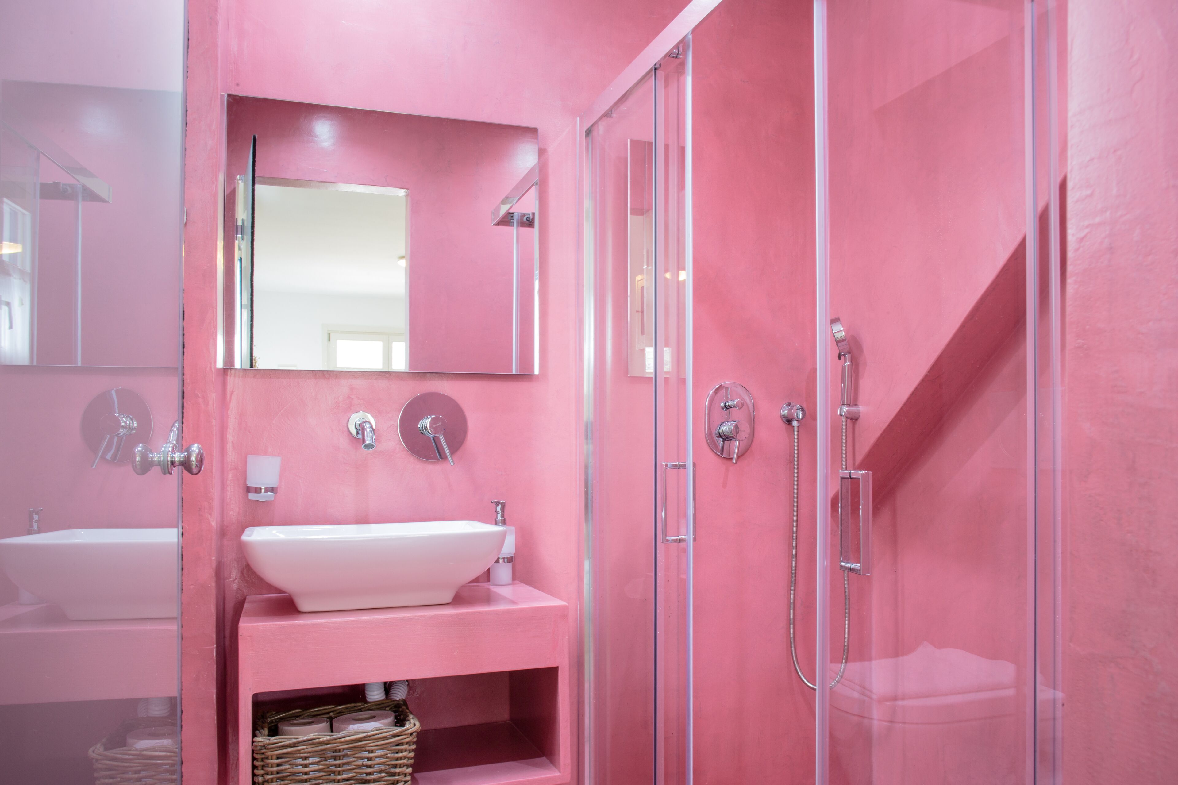 Une salle de bain rose avec un lavabo, un miroir et une douche.
