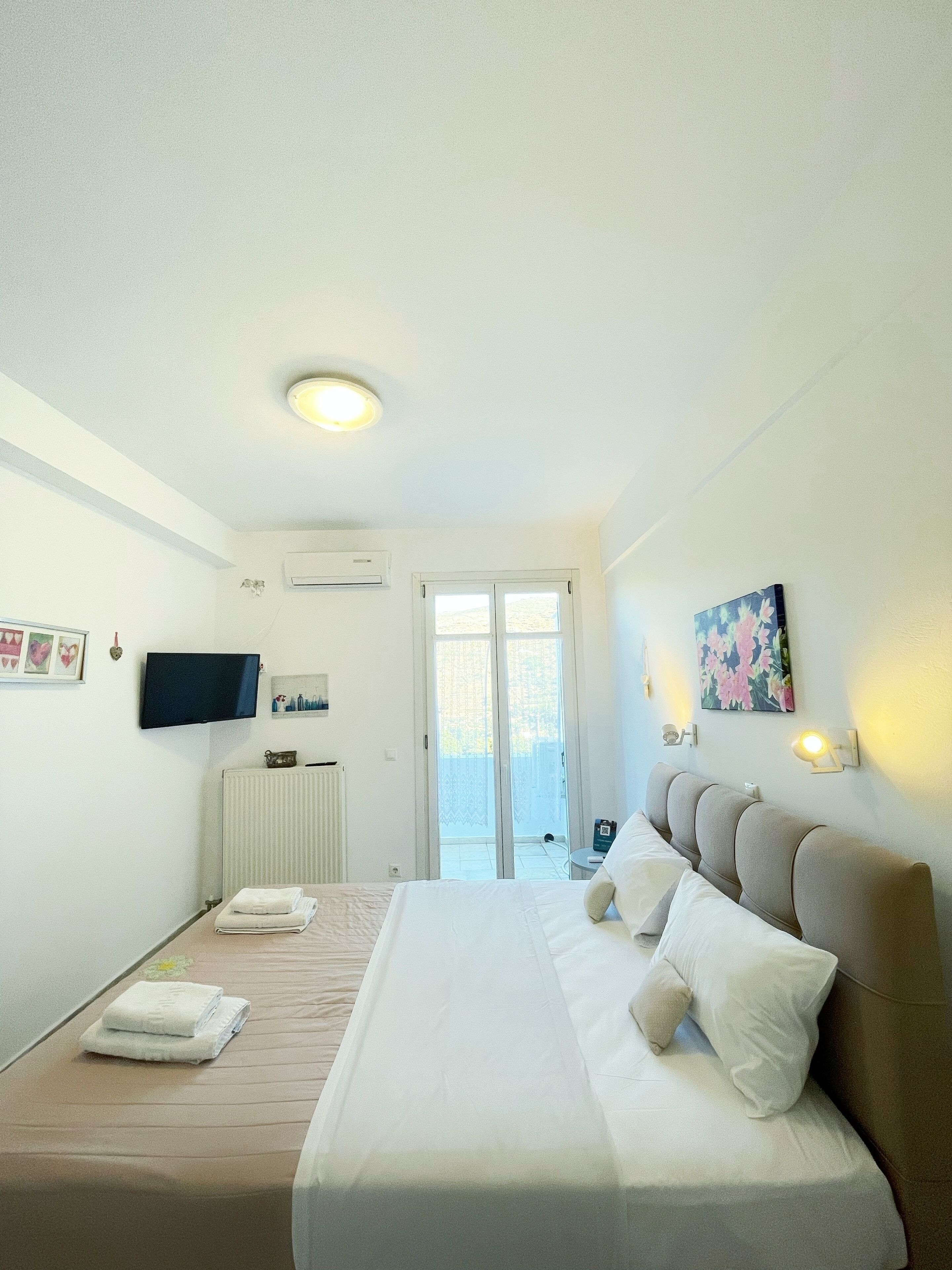 Habitación de hotel con una cama grande, un televisor de pantalla plana, una lámpara de techo, un equipo de aire acondicionado y una puerta corredera de cristal que da a un área exterior.