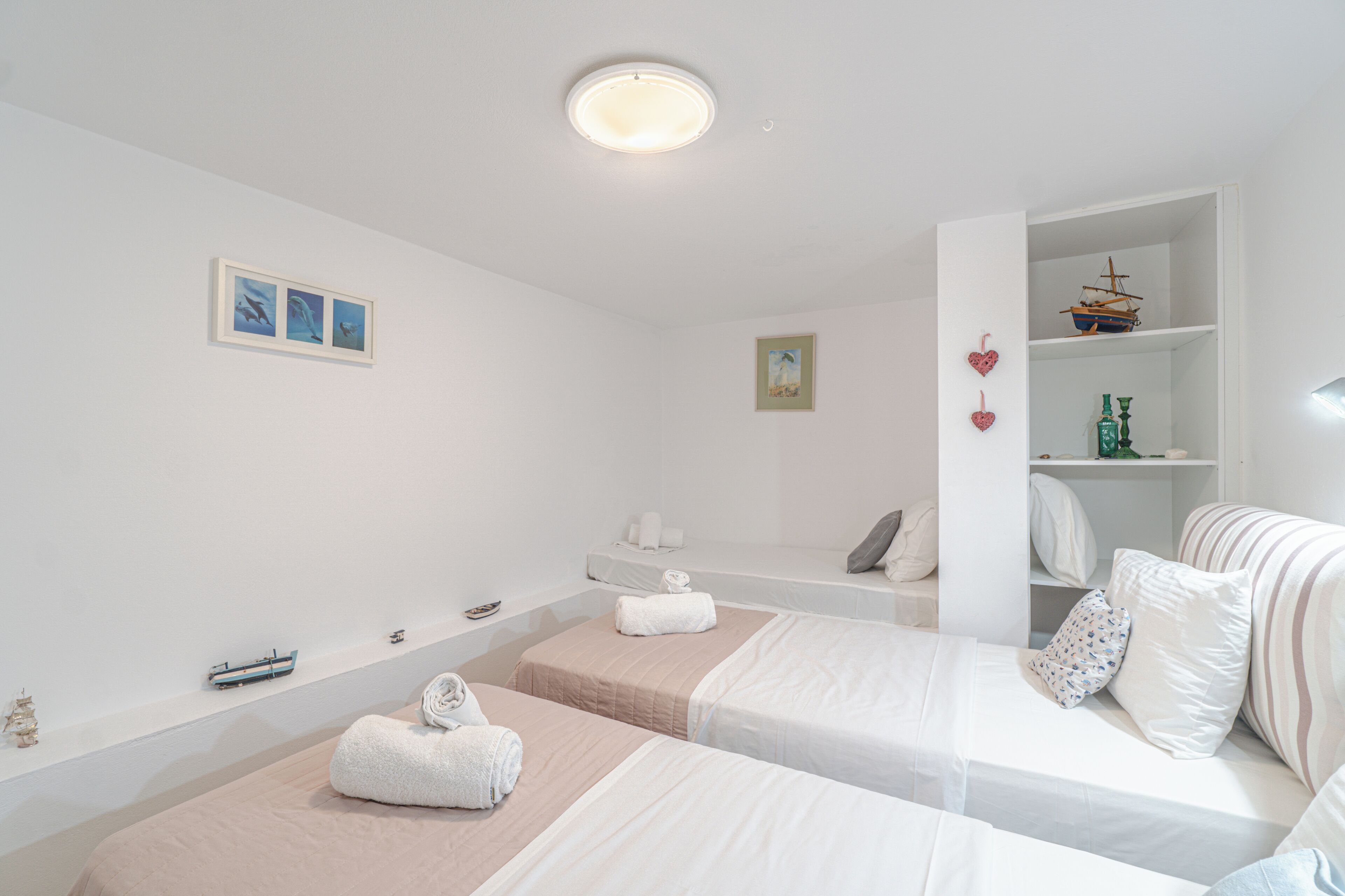 Habitación de hotel con dos camas, una pequeña zona de estar, un estante con adornos e iluminación en el techo.