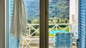 Un balcone con tavolo e sedie, vista su un paesaggio verde e una tenda bianca con un nastro rosso.
