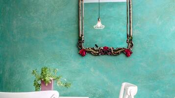 A teal wall with a decorative mirror, white furniture, and a potted plant.