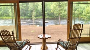 Quarto com duas cadeiras de balanço e uma mesa pequena, com vista para um rio.