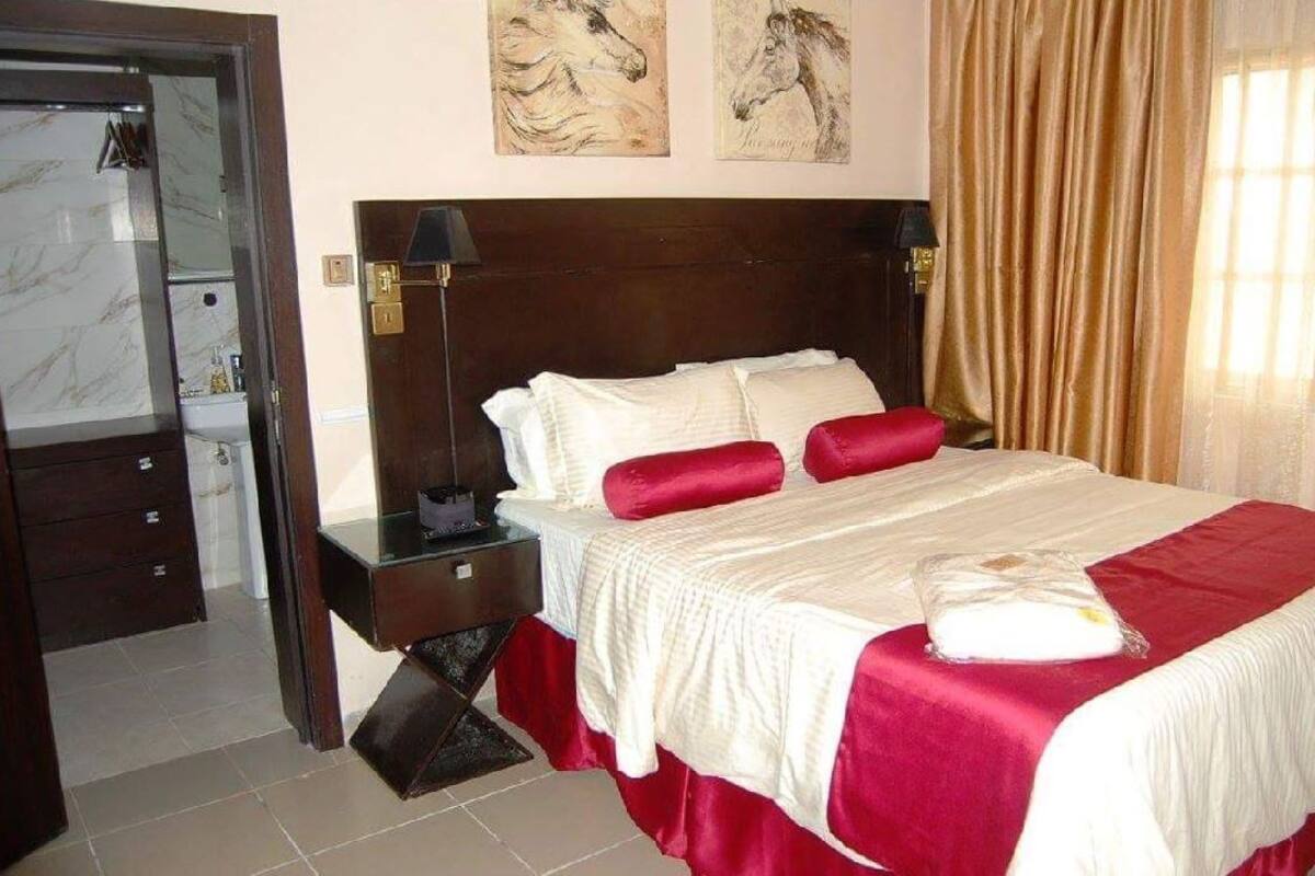 Habitación de hotel con una cama grande, una mesita de noche de madera, un espejo y una puerta que da al baño.