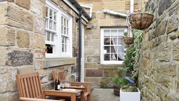 A stone building with wooden furniture and a hanging flower pot. - 2 bedroom accommodation in Skinningrove, near Saltburn-by-the-Sea (Skinningrove, near Saltburn-by-the-Sea)