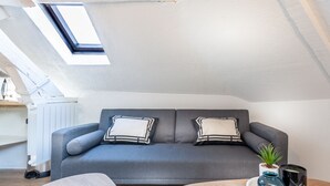 Un salon moderne avec un canapé gris, deux coussins décoratifs, une petite plante en pot et un plateau sur lequel reposent deux vases, le tout sur une table basse en bois.