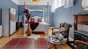Une chambre à coucher avec un lit à baldaquin, une table basse en verre agrémentée d’un service à thé, une chaise en bois et une cheminée.