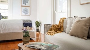 A well-lit room with a bed, a sofa, a small table with a magazine, and two framed pictures on the wall. - Boutique Studio with Balcony in Perfect Location (Lewisham)