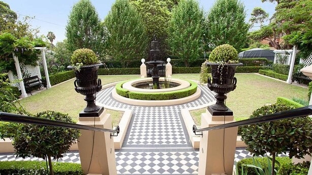 A staircase leading to a circular garden area with a fountain, surrounded by neatly trimmed hedges and trees. - Boutique Studio with Balcony in Perfect Location (Lewisham)