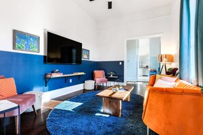 A modern living room with a blue accent wall, a flat-screen TV, a wooden coffee table, and a sofa.