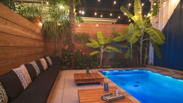 Una zona junto a la piscina con un banco de madera, una mesita con bebidas y la piscina.