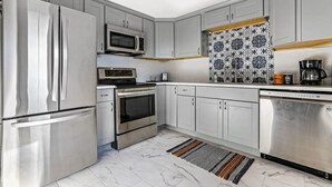 Una cocina moderna con electrodomésticos de acero inoxidable, armarios grises, un salpicadero con estampado y una alfombra a rayas.