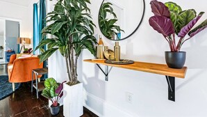 Una sala de estar moderna con un sofá, plantas en macetas, un espejo y un estante de madera con adornos.