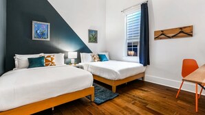 Un dormitorio con dos camas, una ventana con cortinas, una silla de madera y un cuadro en la pared.
