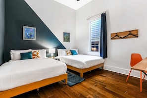 A bedroom with two beds, a window with curtains, a wooden chair, and a wall with a painting.