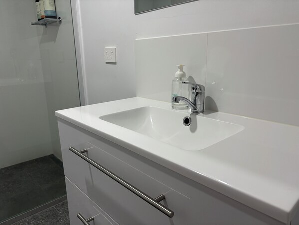 Un baño con un lavabo blanco, un espejo y una botella de jabón para manos.