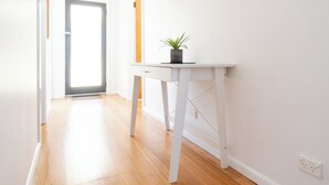 Un pasillo con piso de madera, una mesa blanca con una planta y una puerta al final.