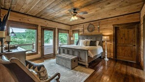 A wooden cabin bedroom with a bed, a desk, a chair, and a window overlooking greenery. - The Haven on Toccoa - River deck | Fire Pit | Hot Tub | Outdoor Fireplace (Blue Ridge)