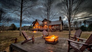 A rustic lodge with a fire pit and Adirondack chairs on a wooden deck. - The Haven on Toccoa - River deck | Fire Pit | Hot Tub | Outdoor Fireplace (Blue Ridge)