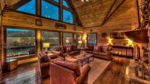 A cozy log cabin interior with a large living area, wooden walls, and large windows offering views of the outdoors. - The Haven on Toccoa - River deck | Fire Pit | Hot Tub | Outdoor Fireplace (Blue Ridge)