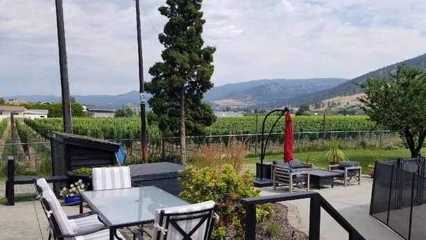 An outdoor patio with a glass table, chairs, and a barbecue area. - Updated Heritage House close to Naramata Bench (Penticton)