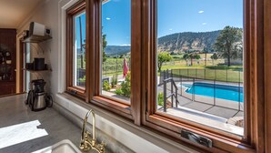 A kitchen with large windows, a coffee maker, and a view of a swimming pool and landscape. - Updated Heritage House close to Naramata Bench (Penticton)