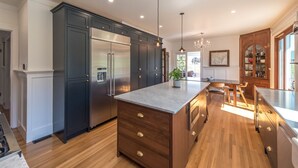 A modern kitchen with dark cabinetry, stainless steel appliances, a marble island, and wooden flooring. - Updated Heritage House close to Naramata Bench (Penticton)