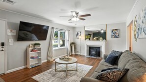Un salon comprenant un canapé, une table basse, un téléviseur, une bibliothèque, une cheminée et un ventilateur de plafond.
