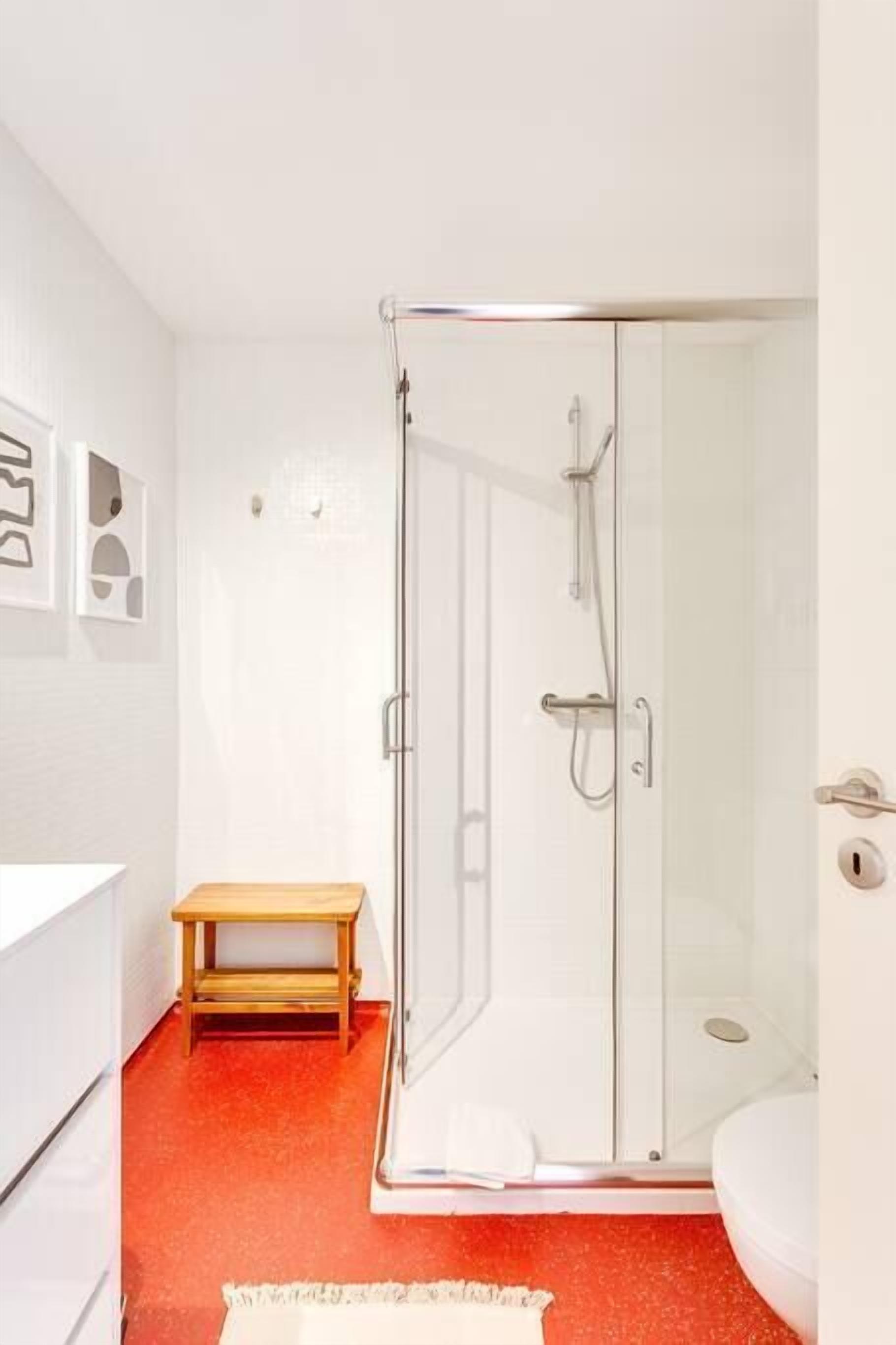 A modern bathroom with a glass shower enclosure, a wooden bench, and a white sink.