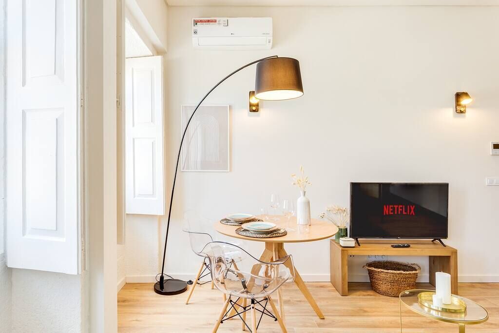 Ein modernes Wohnzimmer mit einem runden Holztisch, transparenten Stühlen, einer Stehlampe, einem Fernseher, der Netflix zeigt, und einem Korb unter dem TV-Schrank.