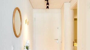 A hallway with a wooden floor, a white door, a mirror, and a small shelf with a plant and a vase. - Boavista Green Studio by DA'HOME (Porto)