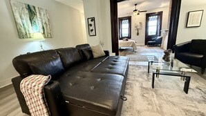 A modern living room with a black leather sofa, a glass coffee table, and a patterned throw blanket. - Large 1BR on hill close to everything in Pitt (Pittsburgh)