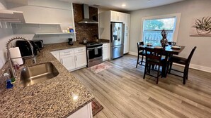 A modern kitchen with granite countertops, stainless steel appliances, and a dining area with wooden chairs and a table. - Large 1BR on hill close to everything in Pitt (Pittsburgh)