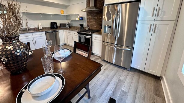 A modern kitchen with white cabinets, stainless steel appliances, and a wooden dining table set for two. - Large 1BR on hill close to everything in Pitt (Pittsburgh)