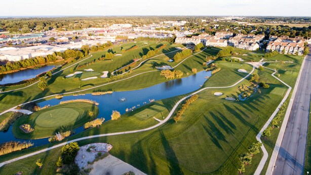 En vy över en golfbana från ovan, med en sjö och bostadshus runt omkring.