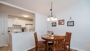 A dining area with a wooden table and chairs, a hanging light fixture, and a kitchen in the background. - Patriots Point a Stylishly decorated duplex -Near MCAS Cherry Point– VERY CLEAN! (Havelock)