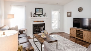 A living room with a fireplace, a sofa, a coffee table, a TV, and a bookshelf. - Patriots Point a Stylishly decorated duplex -Near MCAS Cherry Point– VERY CLEAN! (Havelock)