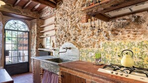 A rustic kitchen with stone walls, a wooden countertop, a gas stove, and a window with a view. - Villa Pera by Nicola Real Estate (Corsanico)