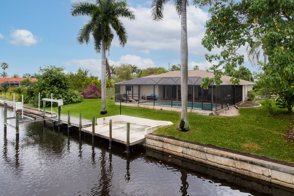 Una casa con piscina, muelle y un jardín césped con palmeras.