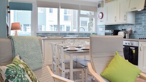 A modern kitchen with white cabinetry, a dining area with a table set for four, and a view of the outside through large windows. - Sanderling - UK32837 (Freshwater East, near Pembroke)