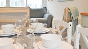 A dining area with white tableware and wine glasses, a grey sofa, and a wooden bench. - Sanderling - UK32837 (Freshwater East, near Pembroke)