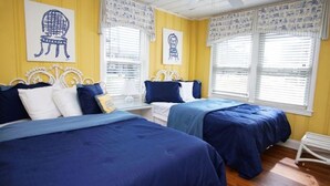 A hotel room with two beds, a white metal headboard, and a window with blinds.